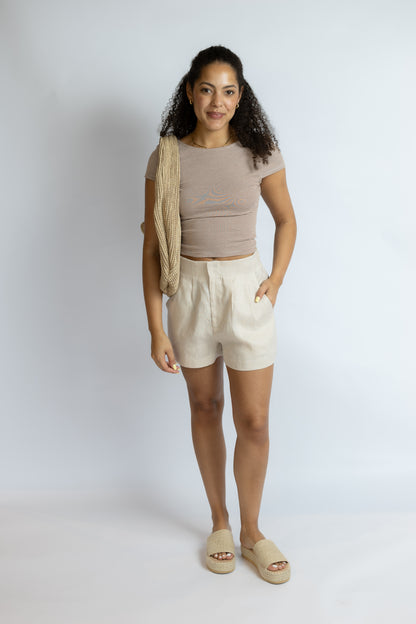 Woman wearing a beige top and shorts with a beige bag on a white background
