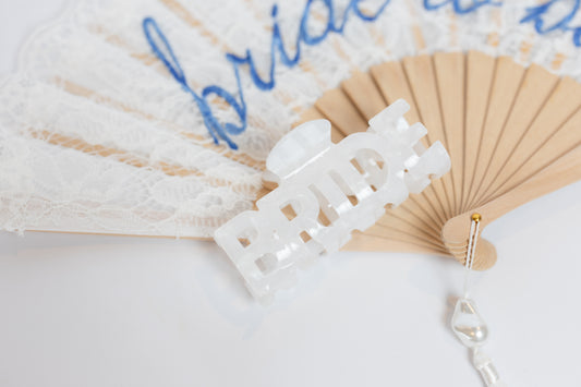 White lace hair clip on a beige fan with 'bride' text on a light background
