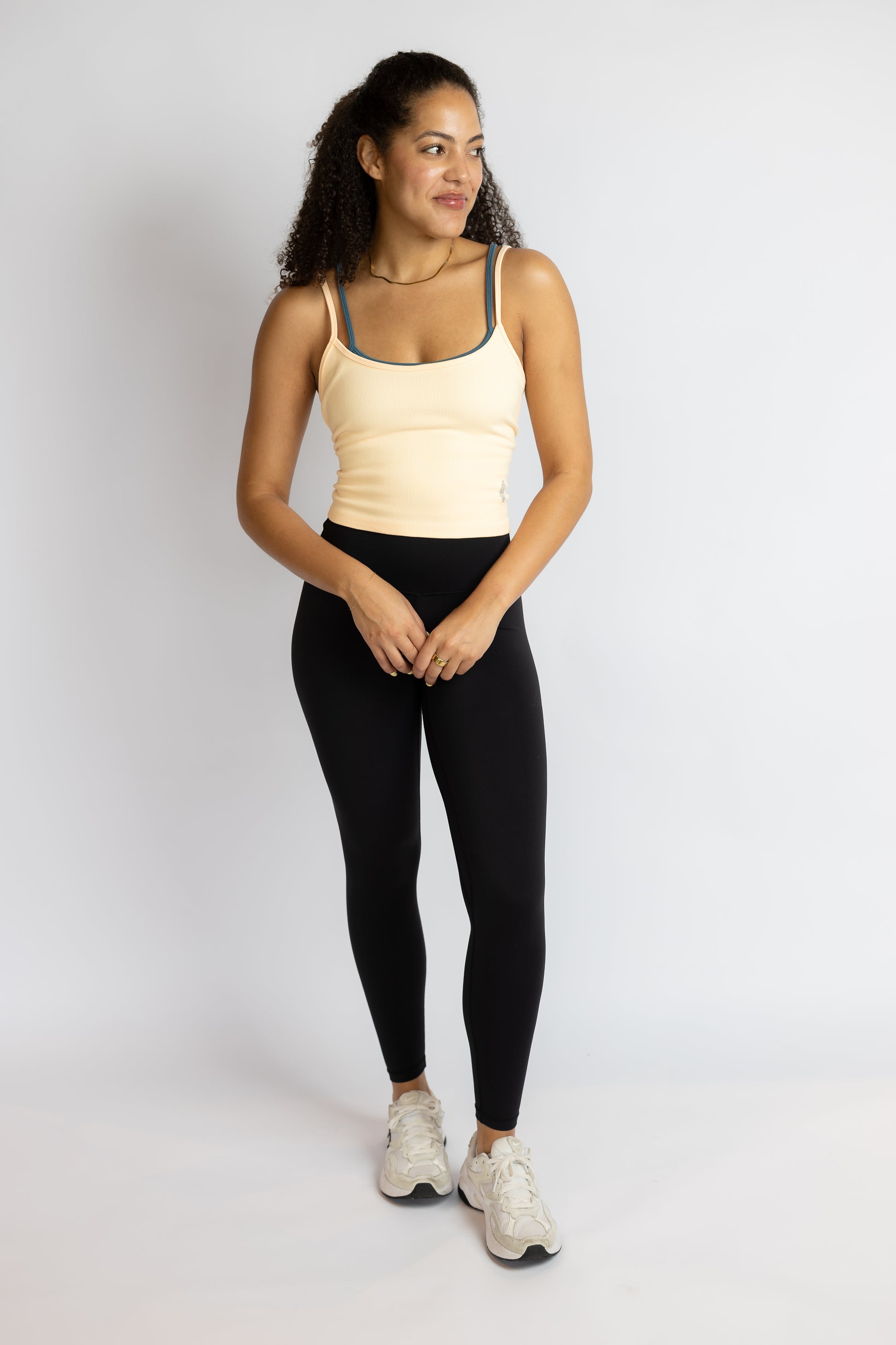 Woman wearing a beige tank top and black leggings on a white background