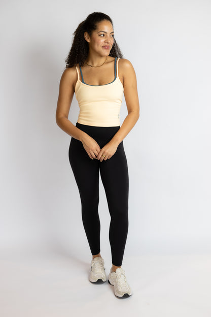 Woman wearing a beige tank top and black leggings on a white background
