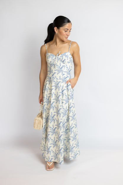 Woman wearing a floral dress holding a handbag against a white background