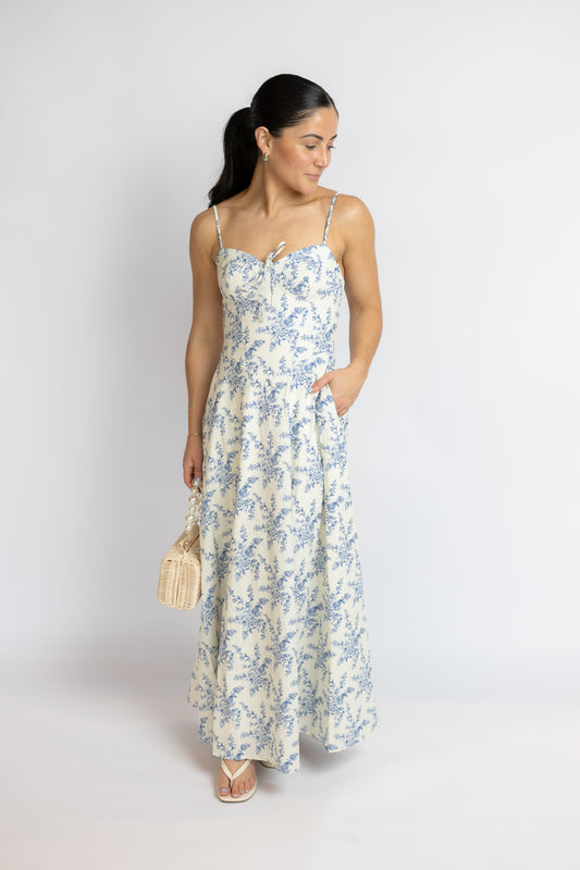 Woman wearing a floral dress holding a handbag against a white background