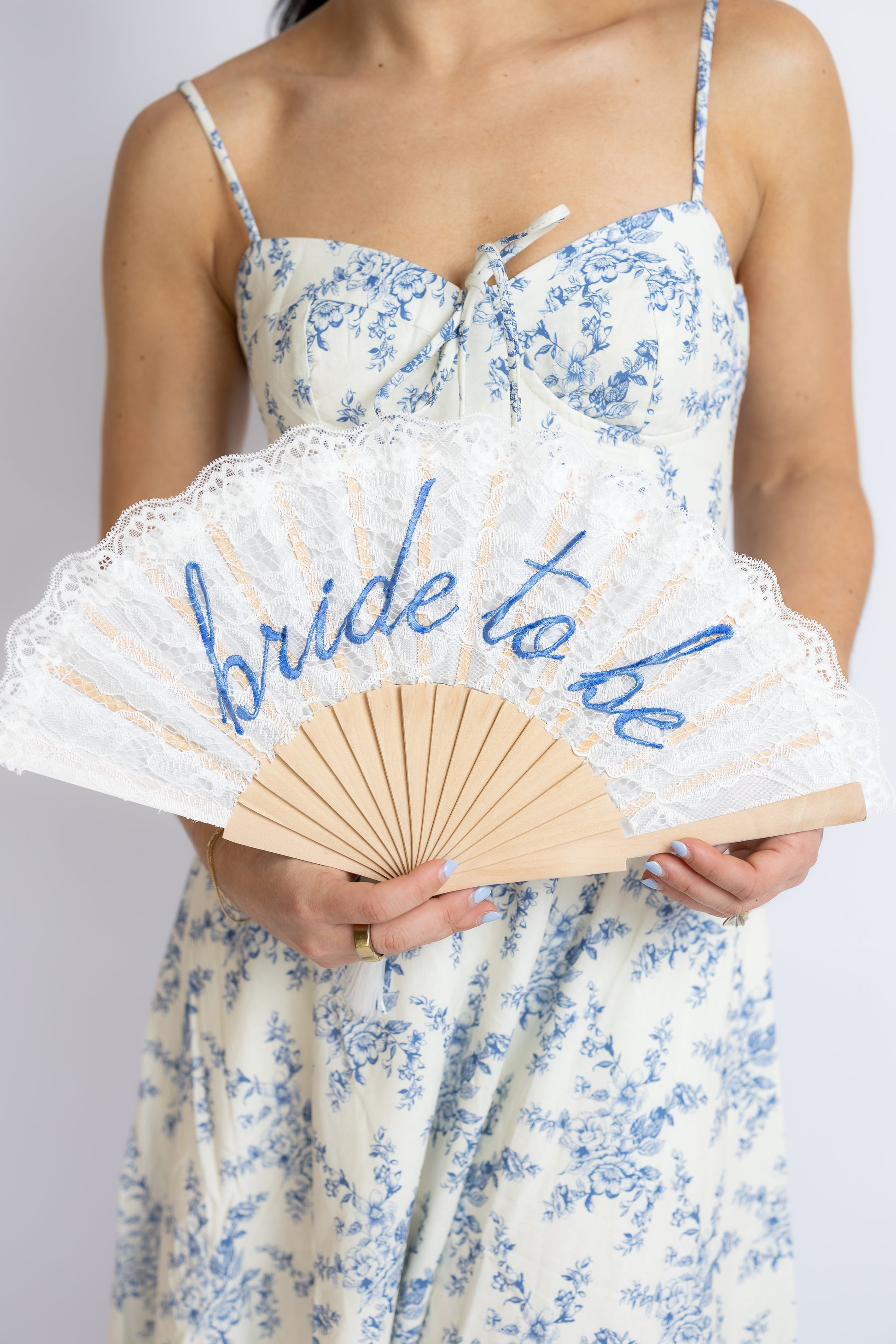 Woman holding a 'bride to be' fan with a white and blue floral dress.