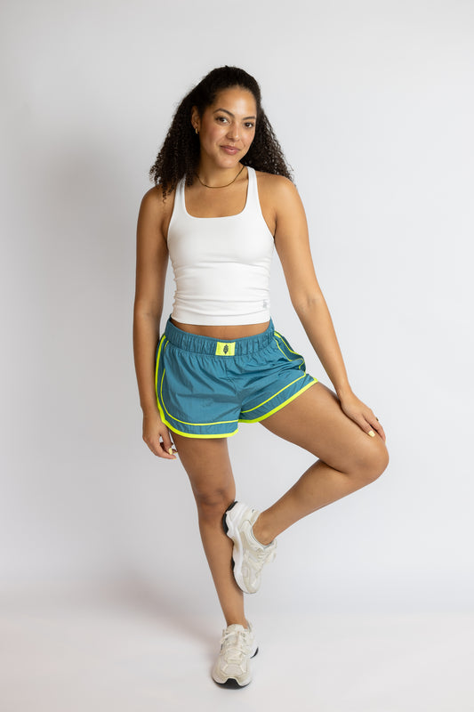 Woman wearing a white tank top and blue shorts with green accents on a white background