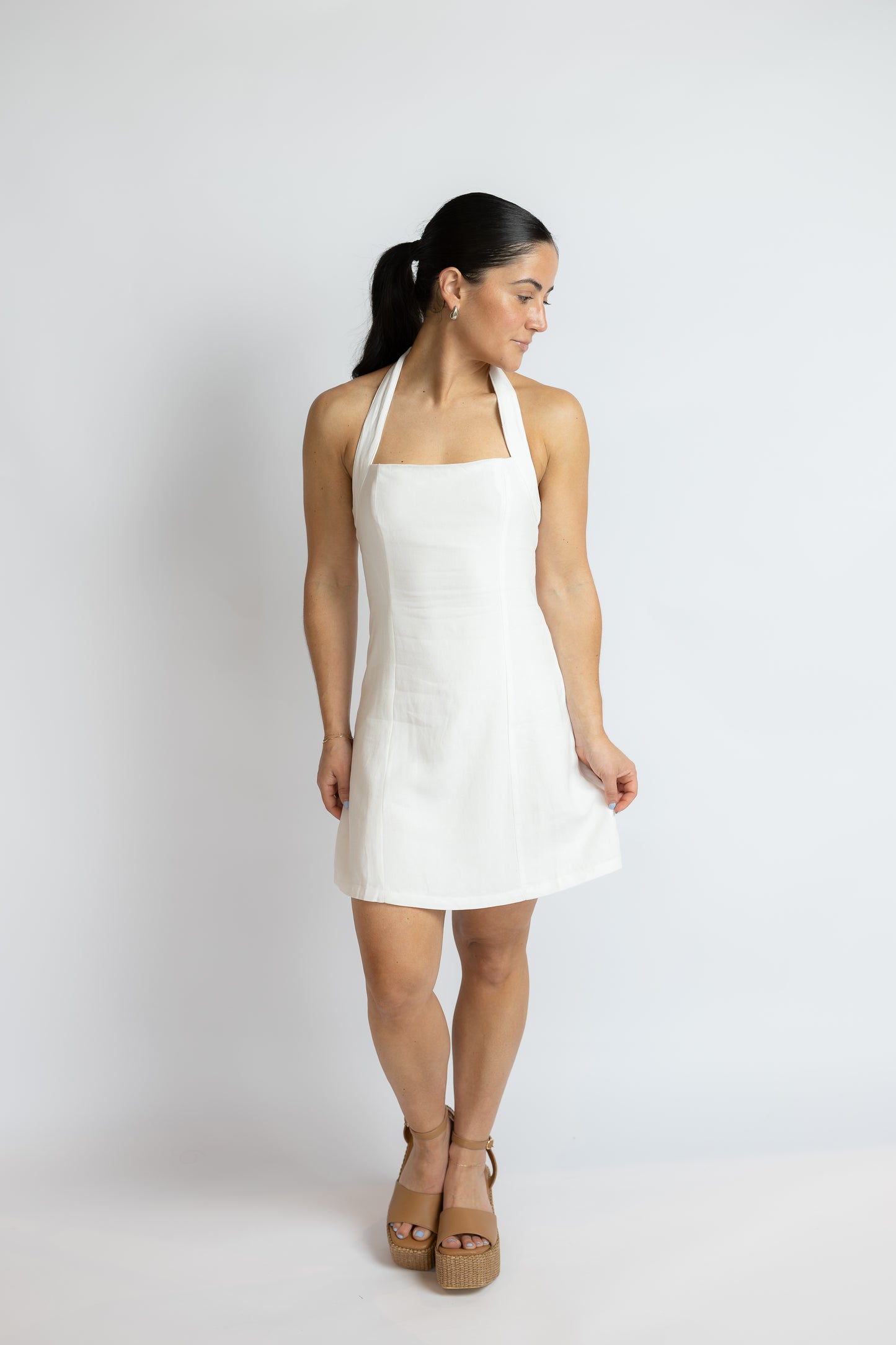 Woman wearing a white halter dress on a plain background