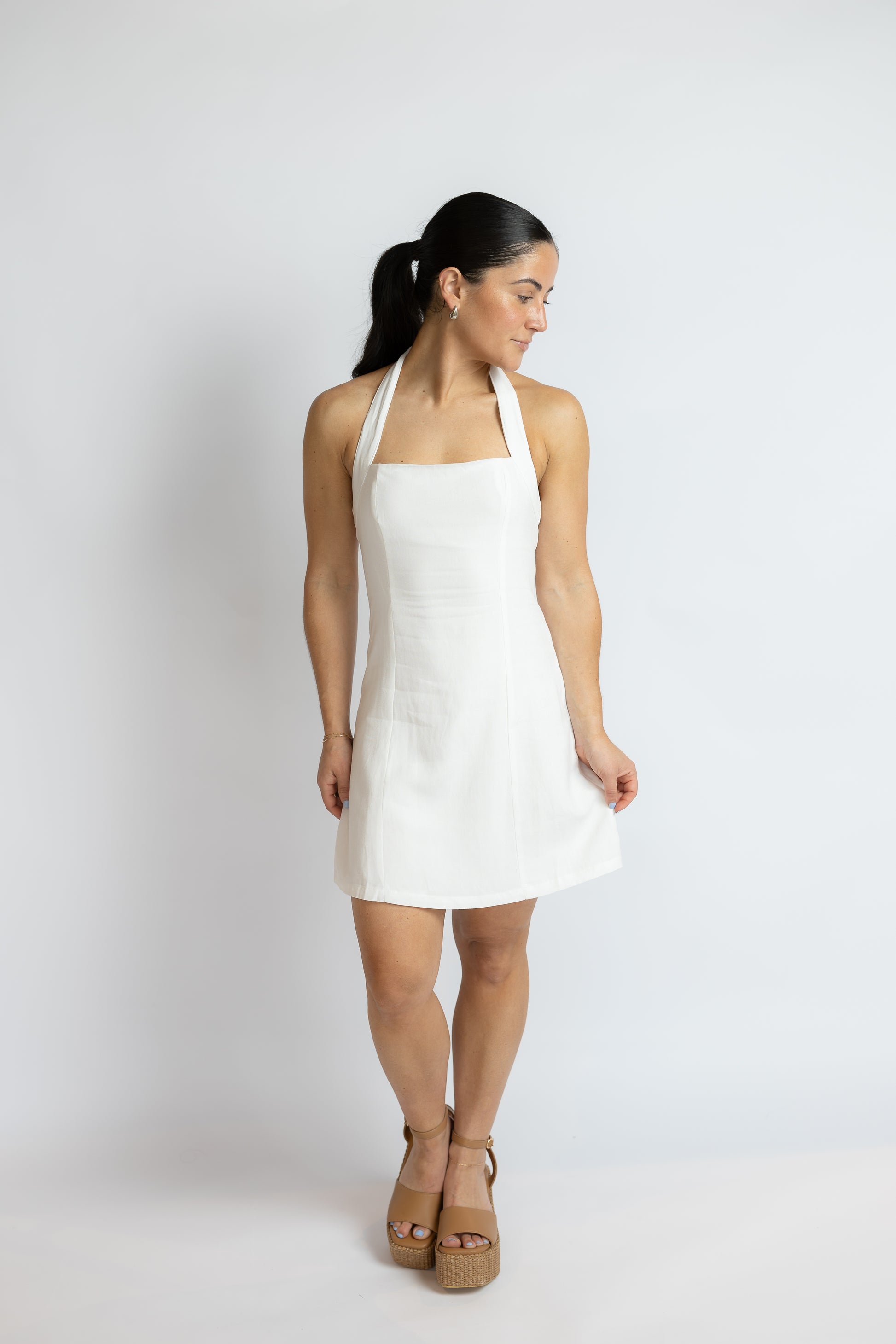 Woman wearing a white halter dress on a plain background