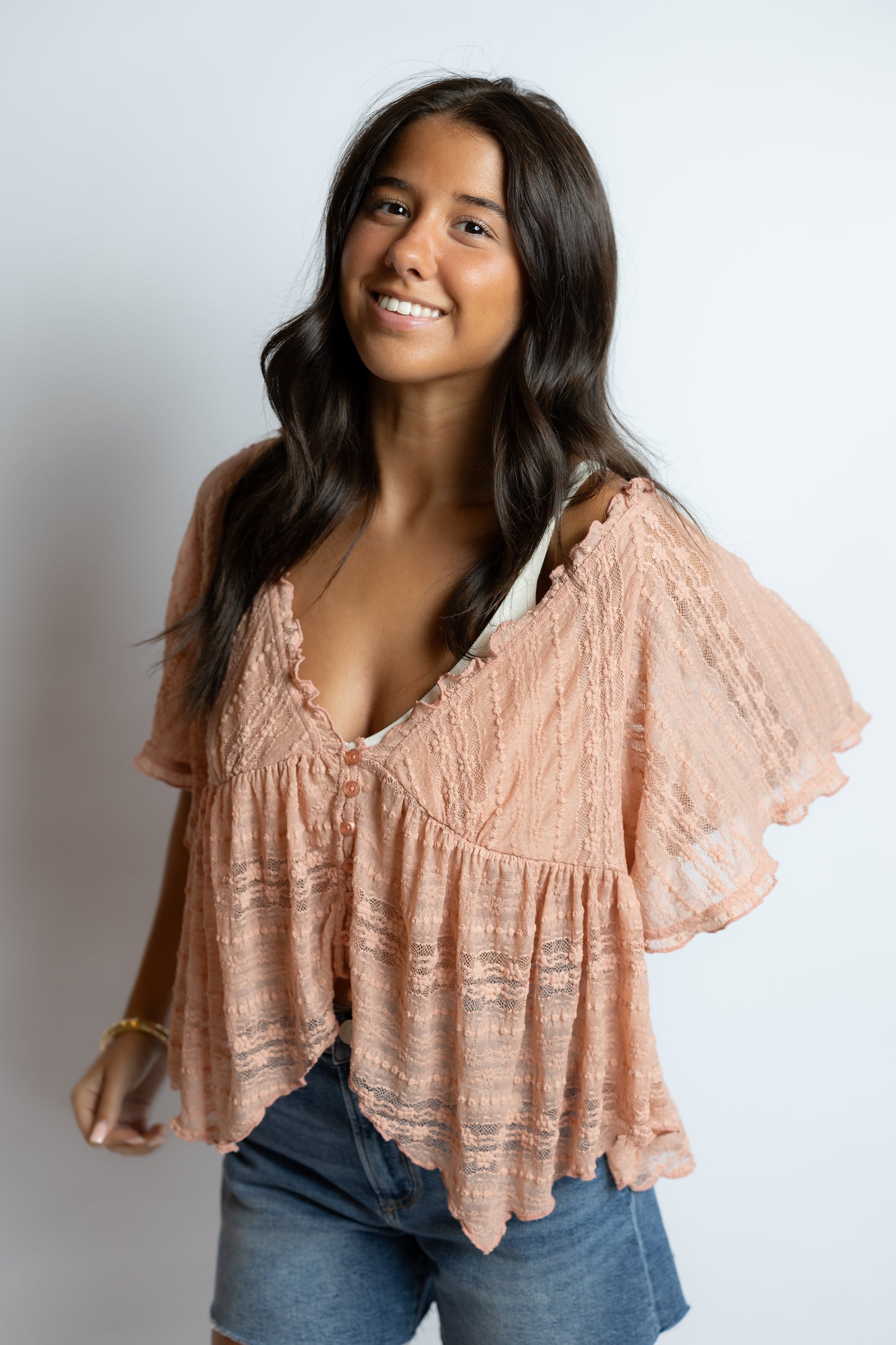 Woman wearing a pink blouse with ruffled sleeves against a plain background