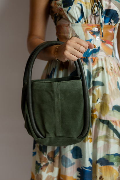 Person holding a green handbag with a floral dress in the background