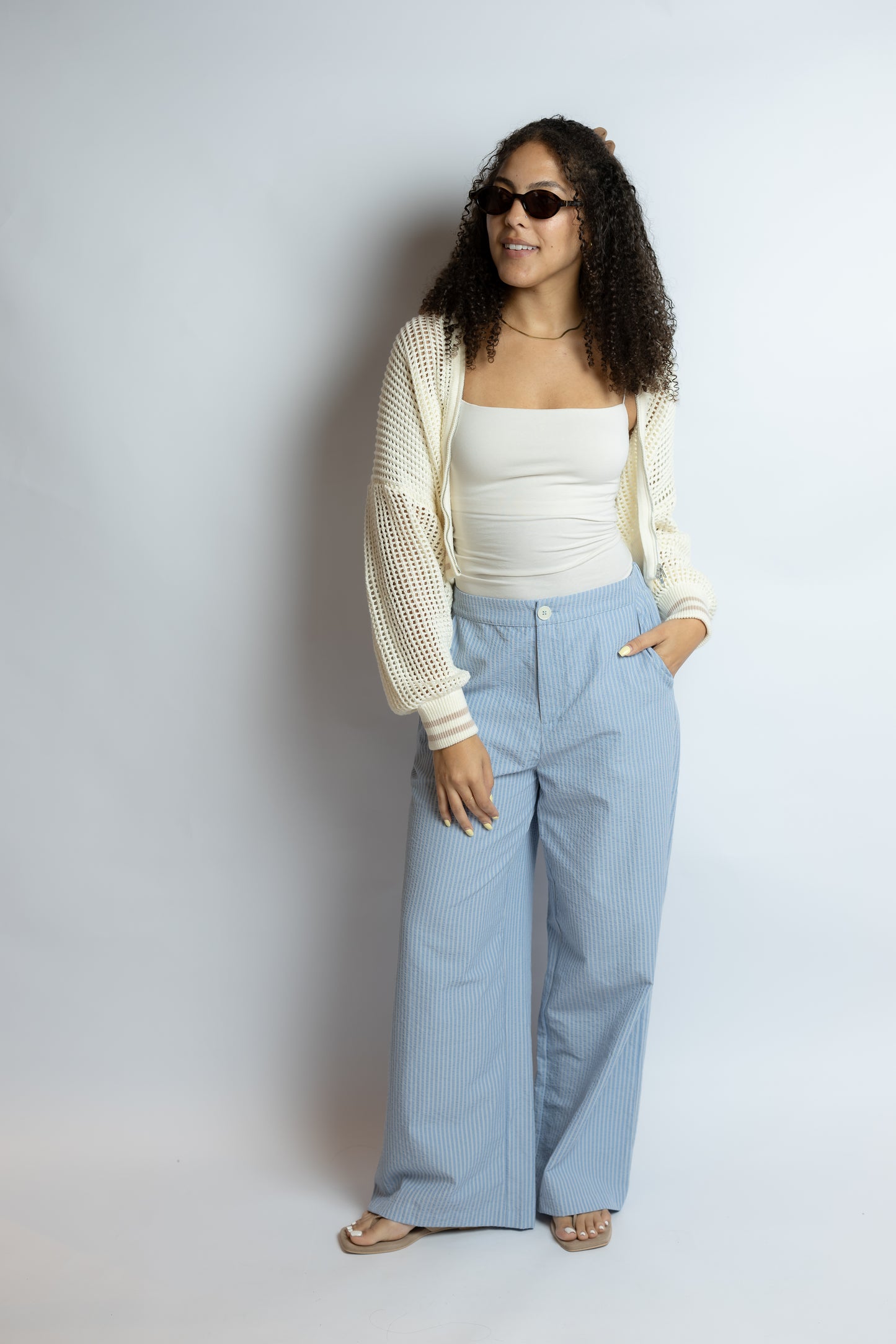 Woman wearing a white top, light cardigan, and blue pants against a plain background