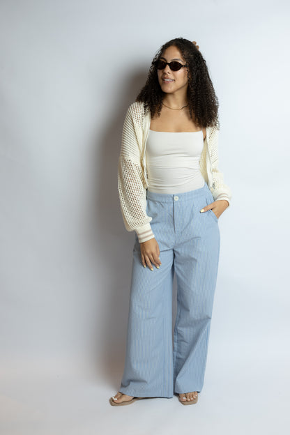 Woman wearing a white top, light cardigan, and blue pants against a plain background