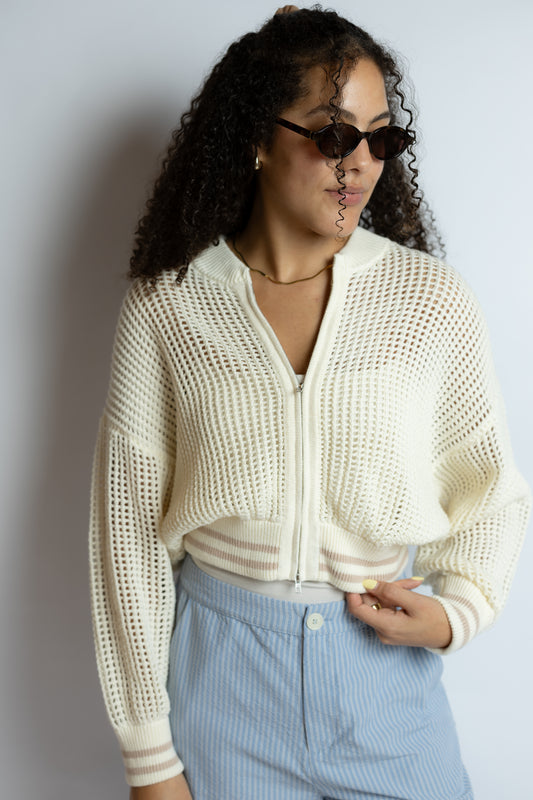 Woman wearing a cream knitted cardigan and light blue pants against a plain background