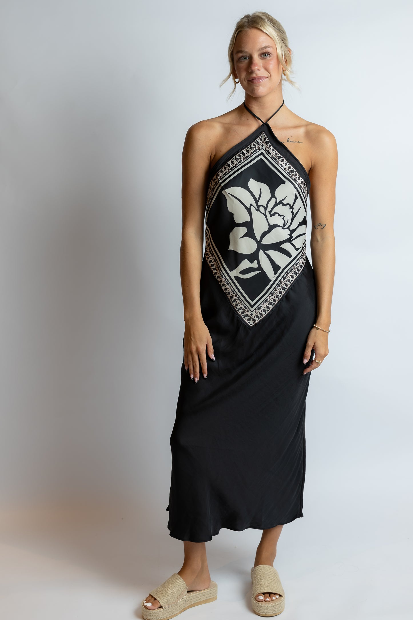 Woman wearing a black halter neck dress with white floral pattern on a plain background