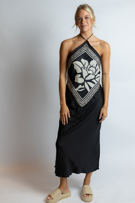 Woman wearing a black halter neck dress with white floral pattern on a plain background
