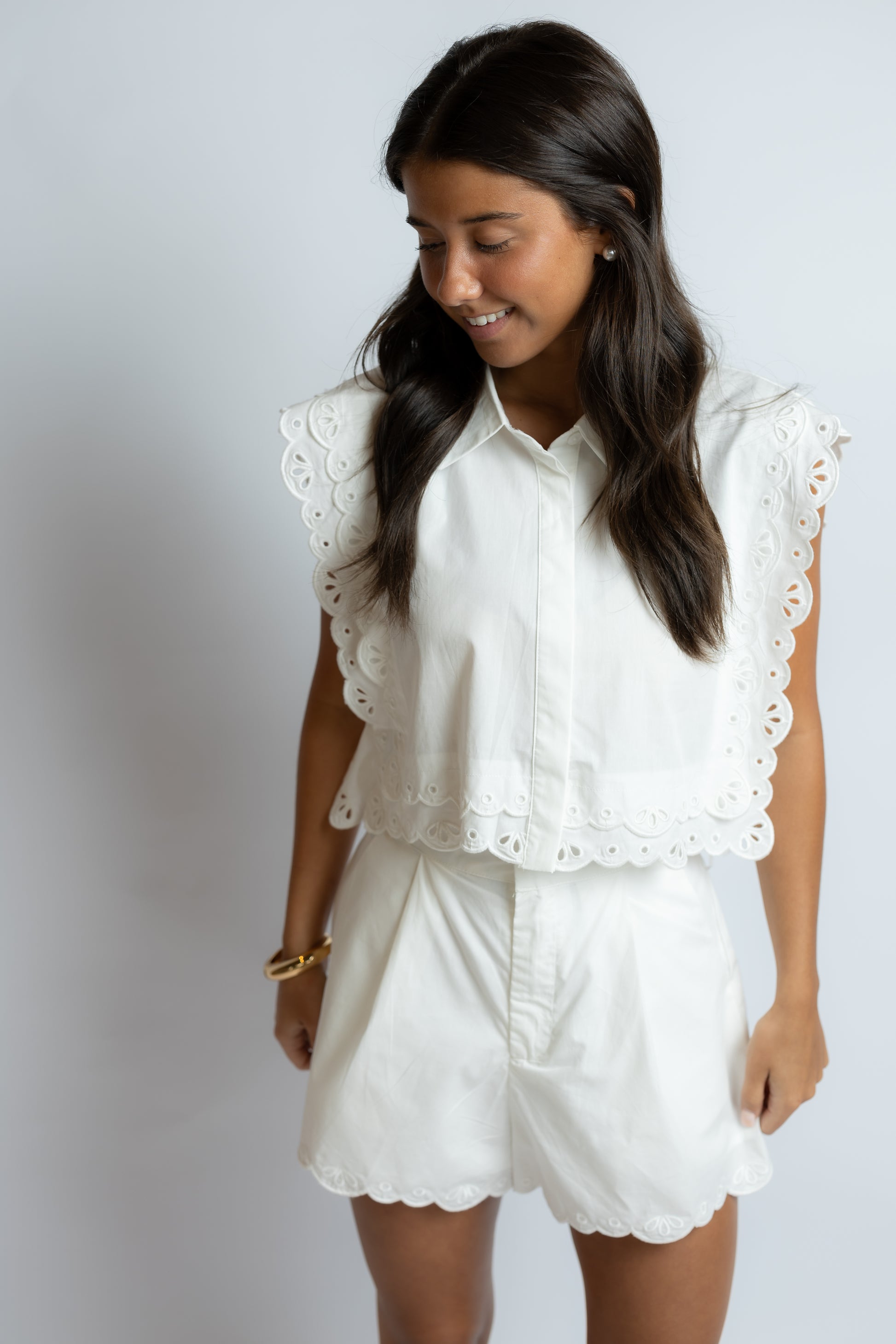 Woman wearing a white blouse with lace details and matching shorts on a plain background