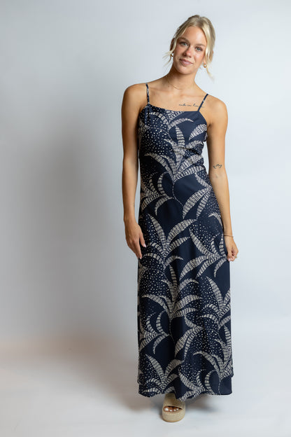 Woman wearing a long navy dress with white patterns on a plain background