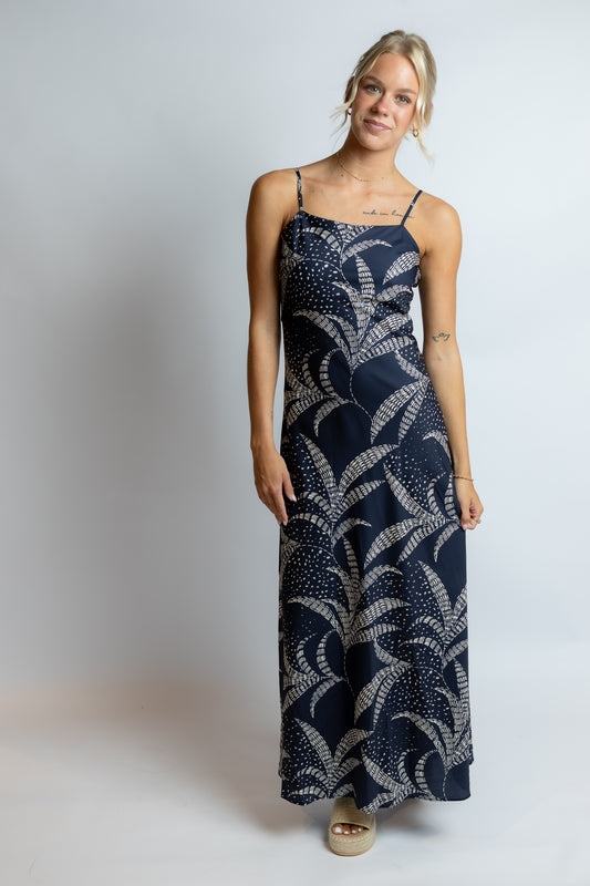 Woman wearing a long navy dress with white patterns on a plain background