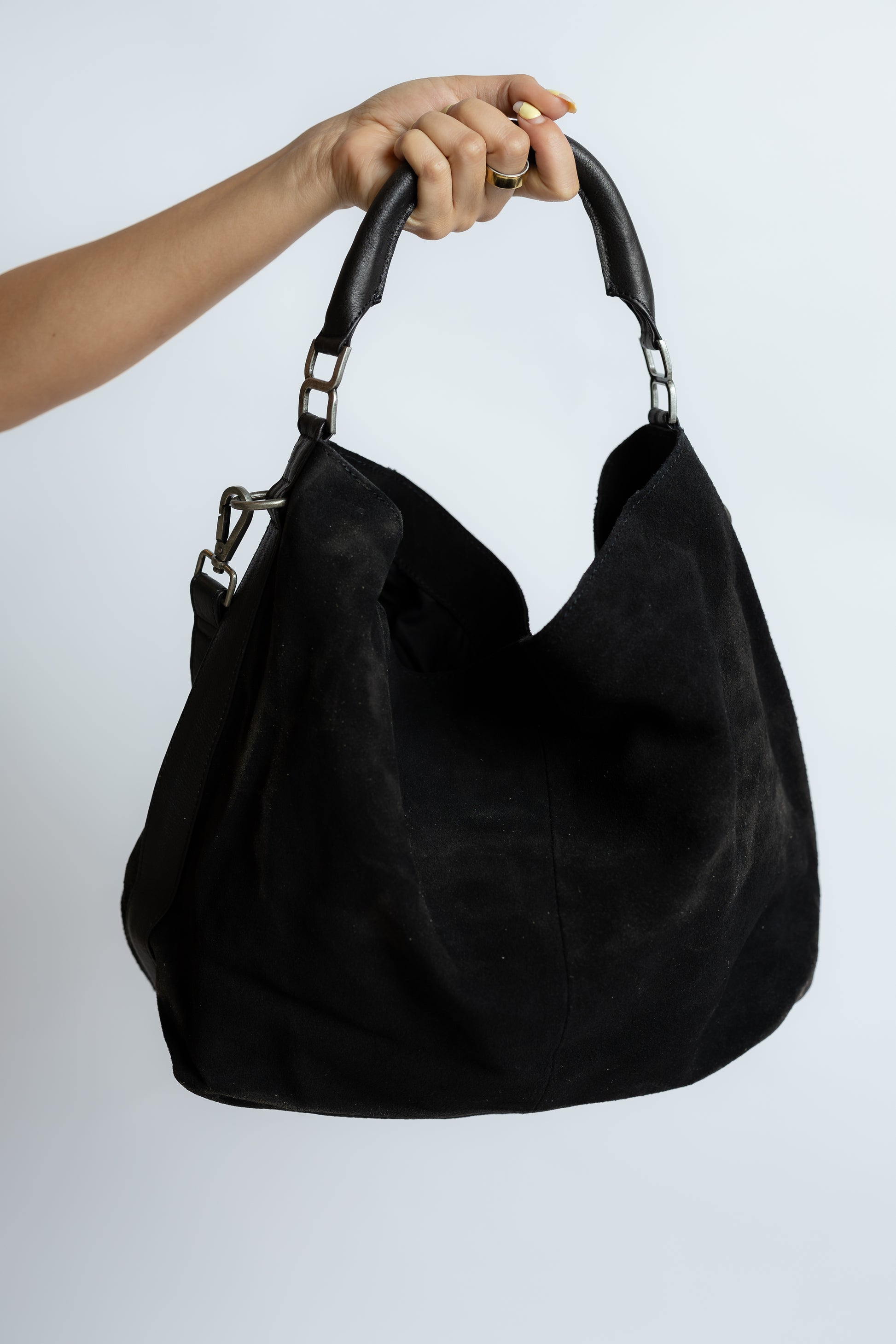 Black handbag held by a hand against a white background