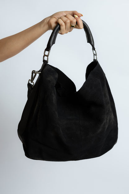 Black handbag held by a hand against a white background