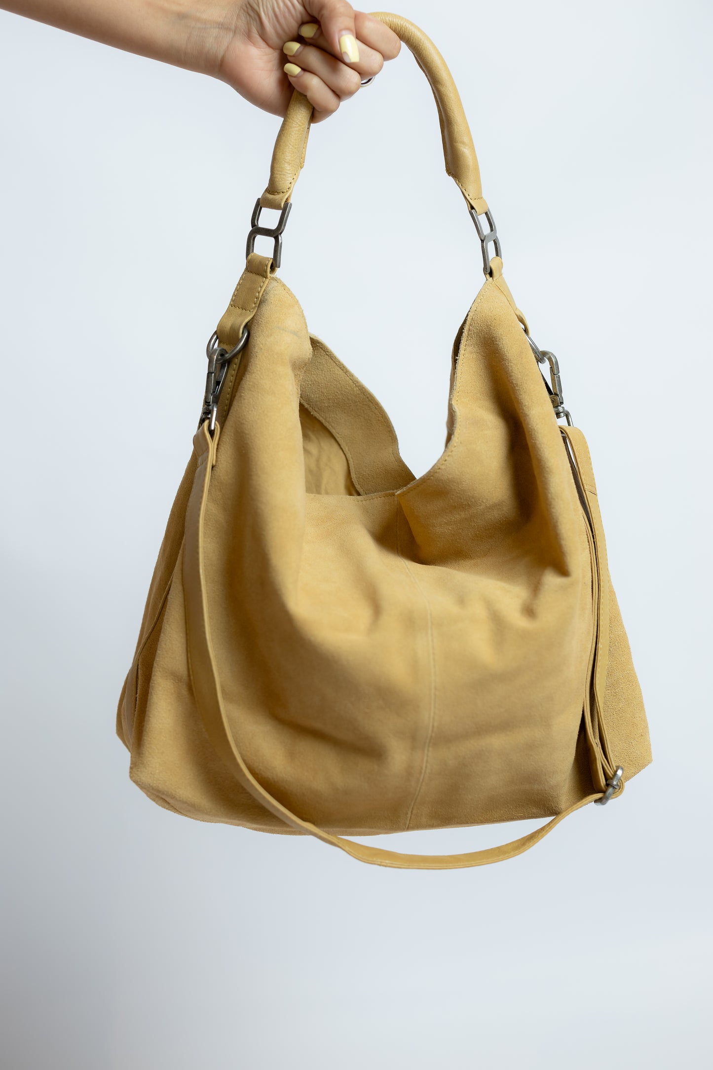 Beige handbag held by a hand against a light gray background