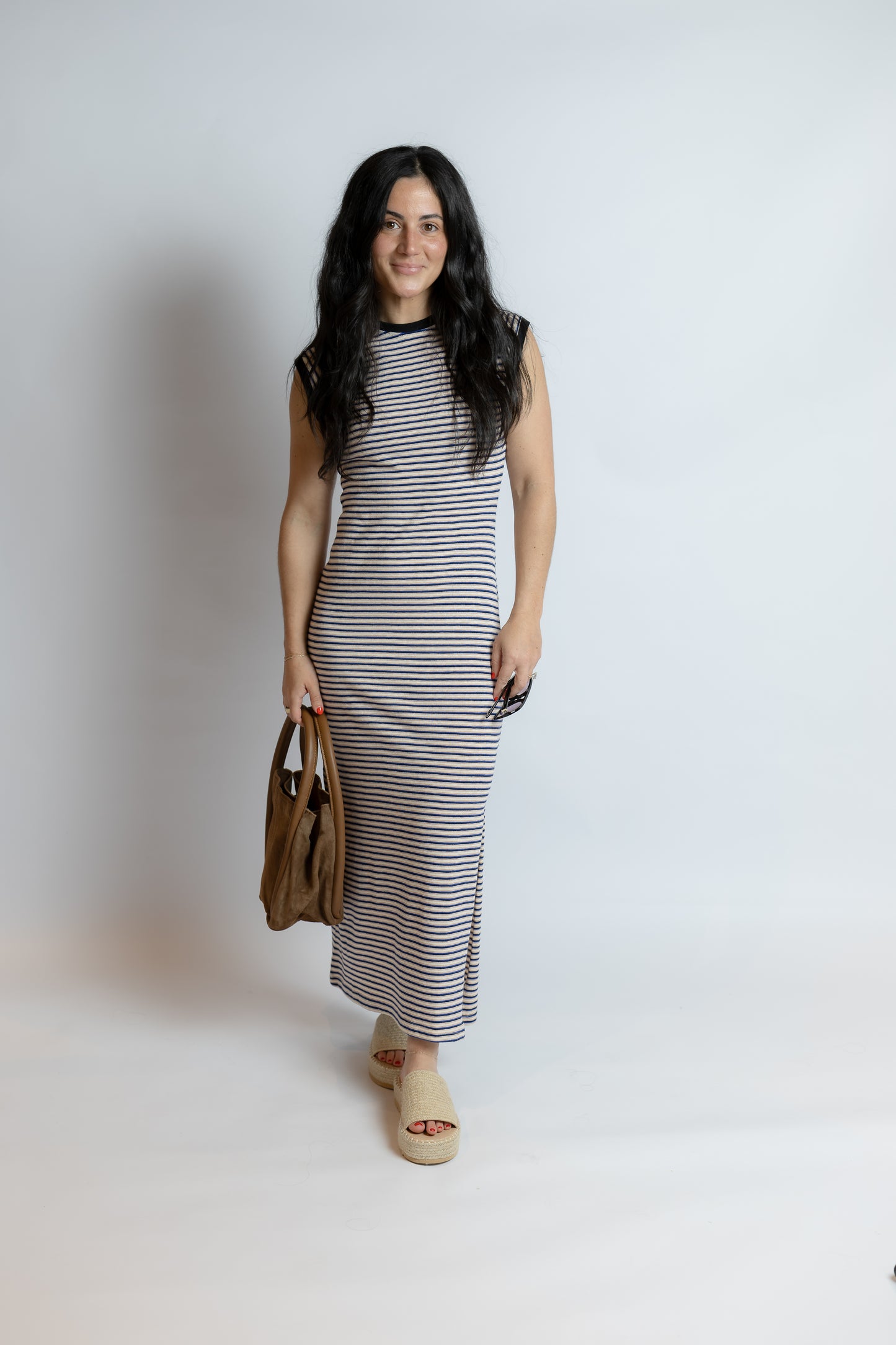 Model wearing the Caspian Knit Dress, a navy and cream striped sleeveless midi dress featuring a crew neckline, contrast trim, side slit detail, and relaxed knit silhouette.