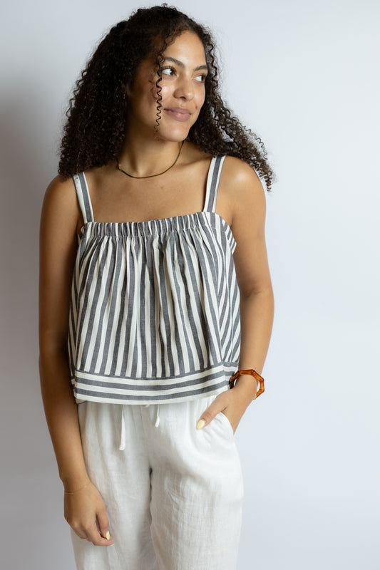 Woman wearing a striped tank top and white pants against a plain background