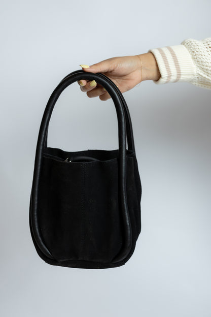 Black suede bucket handbag held by a hand against a light gray background
