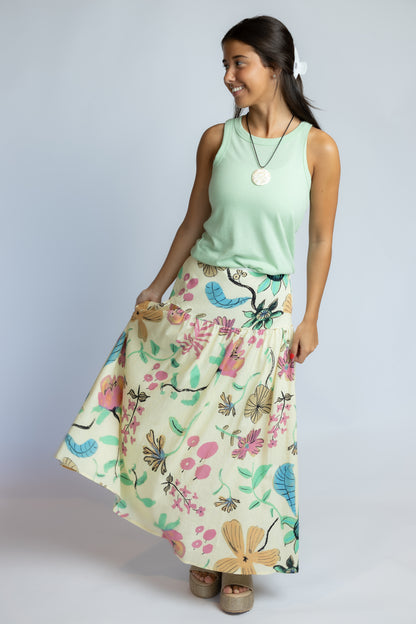 A woman modeling a sleeveless mint green top and a high-waisted, flowing maxi skirt with a colorful floral and butterfly print on a light cream background, set against a plain light gray studio background.