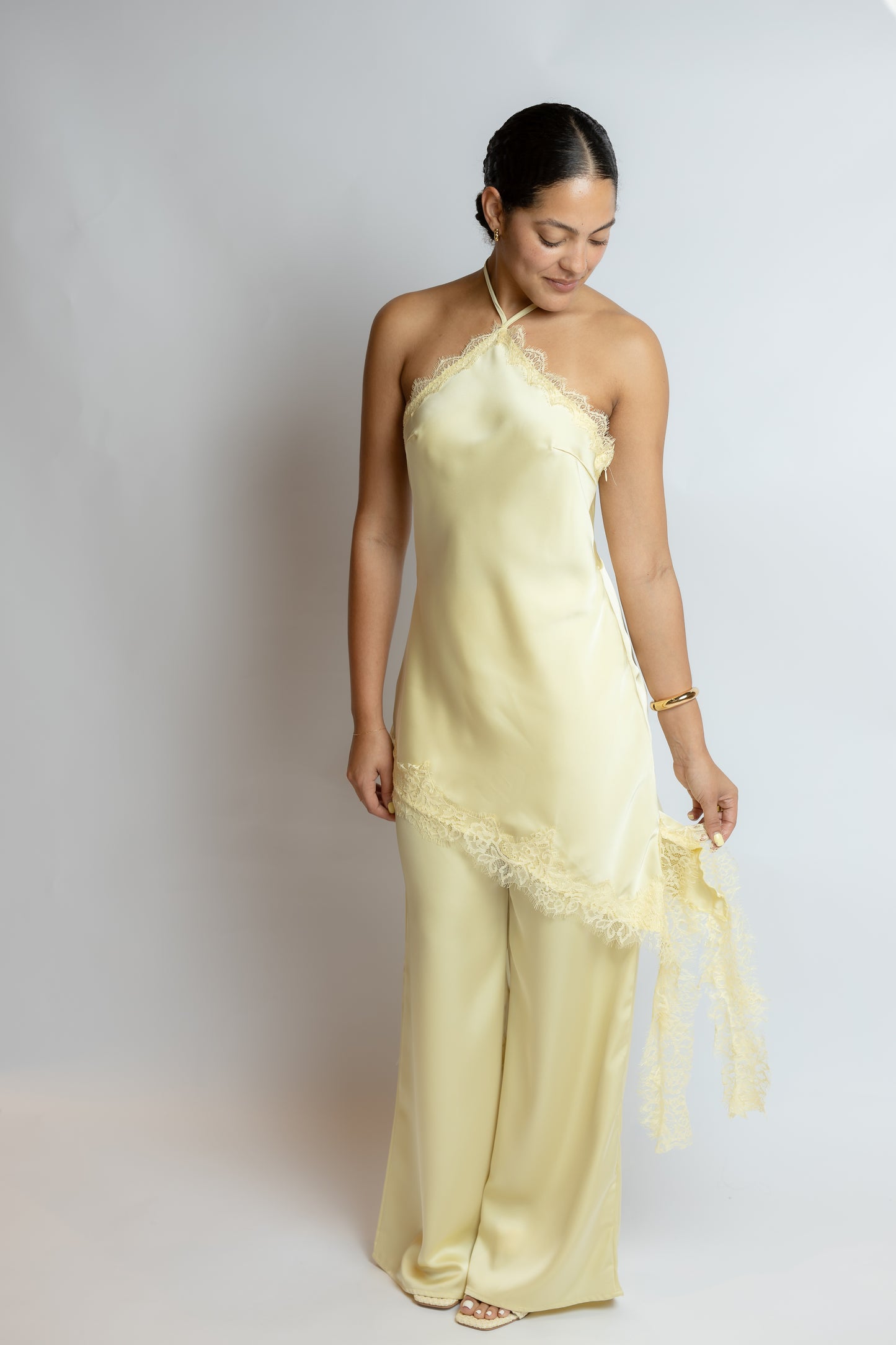 Woman wearing a light yellow slip two piece set with lace details on a plain background