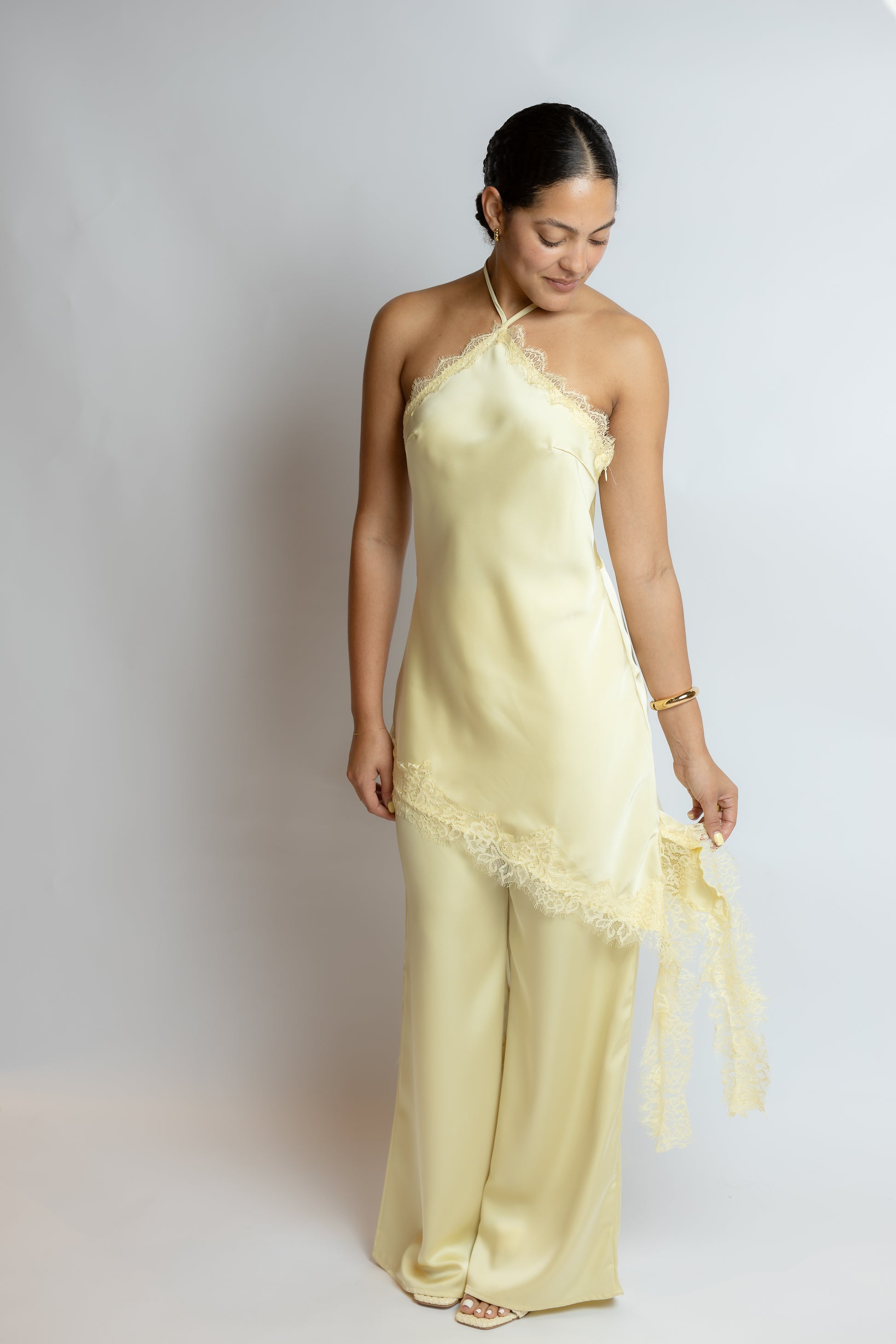 Woman wearing a light yellow slip two piece set with lace details on a plain background