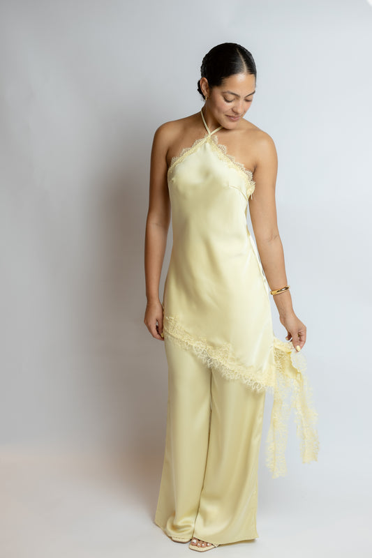 Woman wearing a light yellow slip two piece set with lace details on a plain background