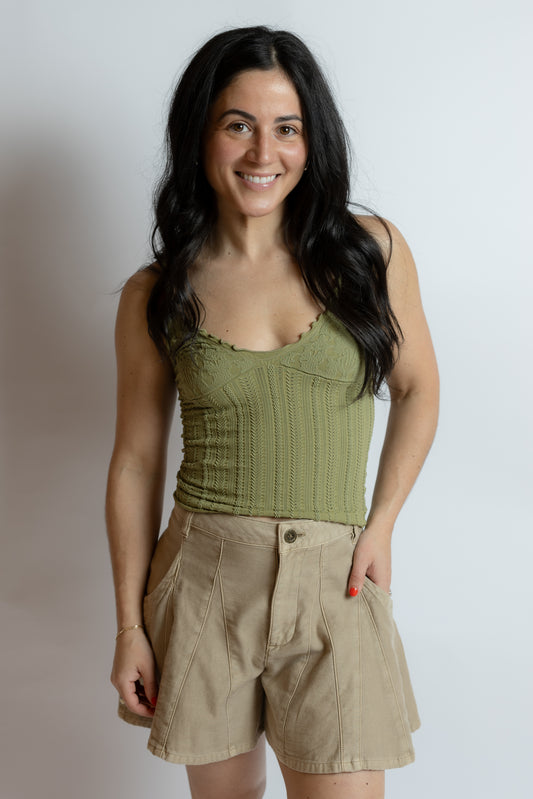 Woman wearing a green tank top and beige shorts against a plain background