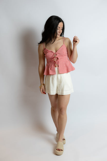 Woman wearing a red checkered top and white shorts on a plain background