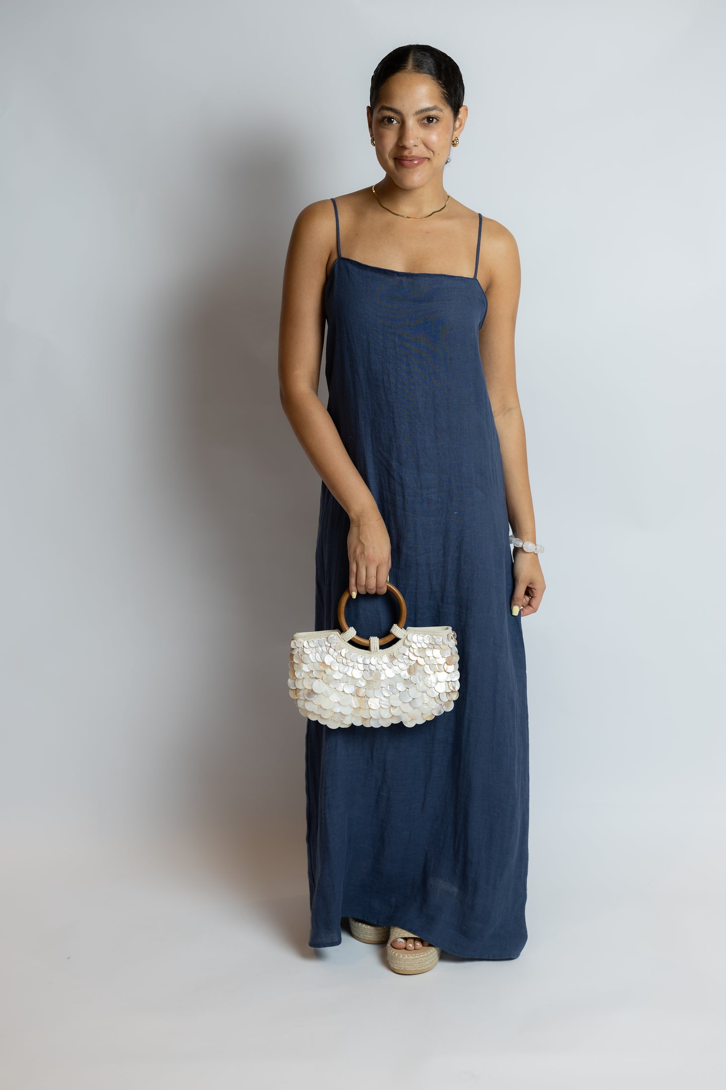 Woman in a blue dress holding a white beaded handbag against a plain background