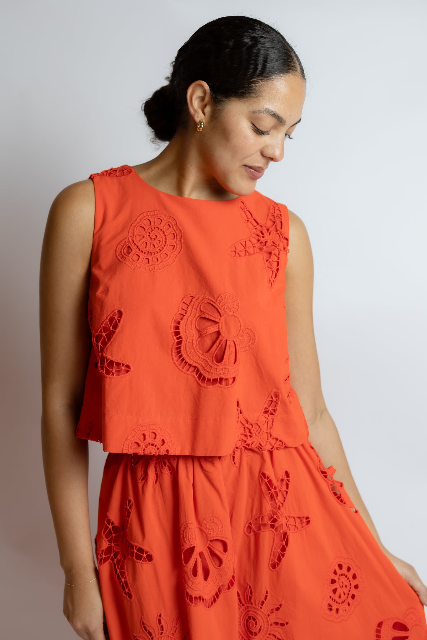 Woman wearing an orange embroidered two piece top and skirt against a plain background