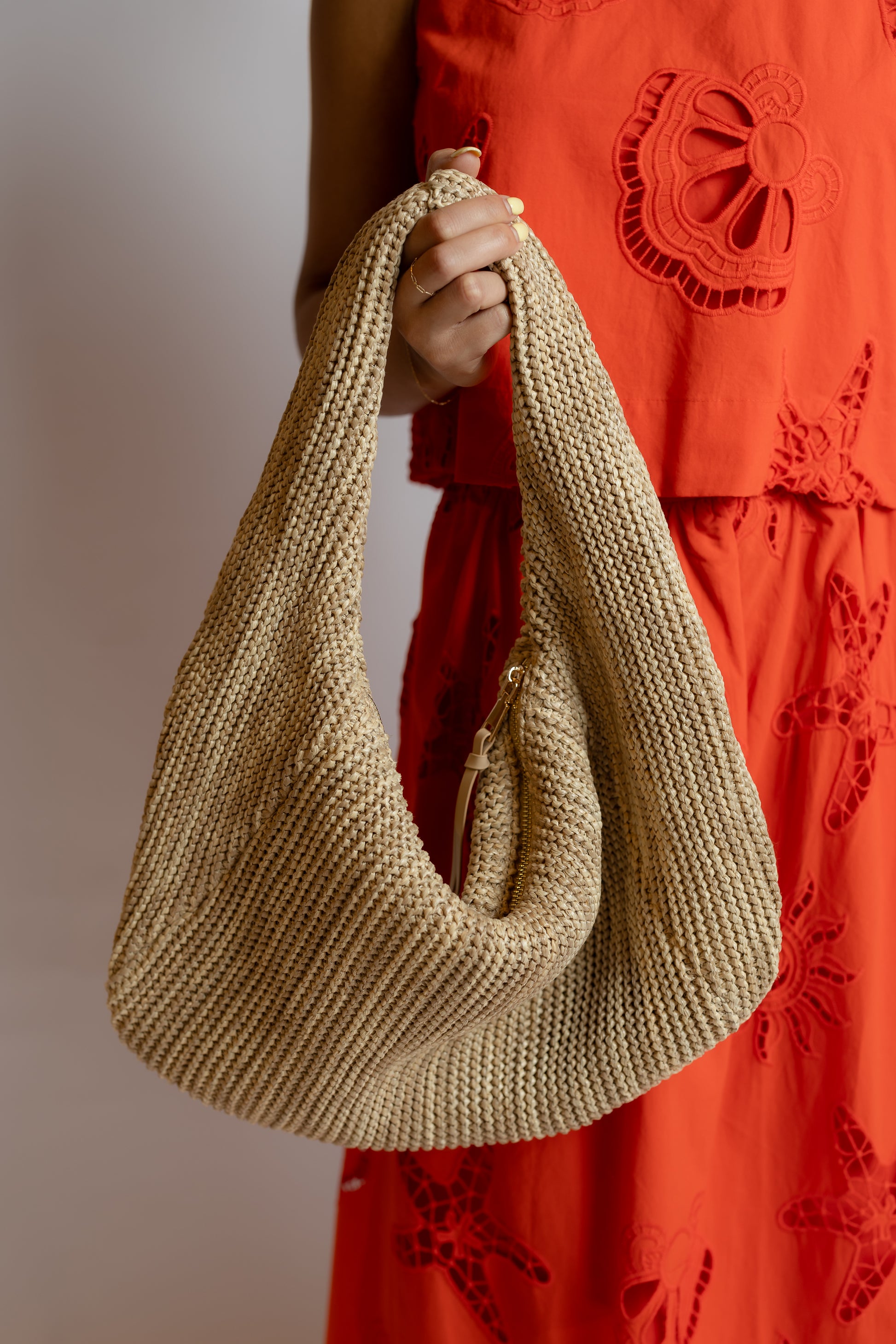 Beige knitted handbag held by a person wearing an orange dress with floral patterns.