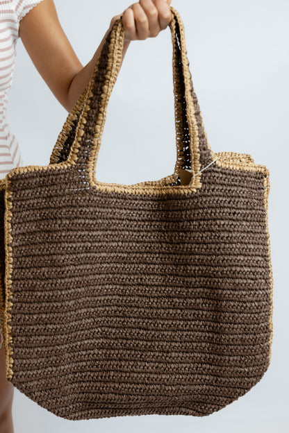 Brown woven tote bag held by a person against a light background