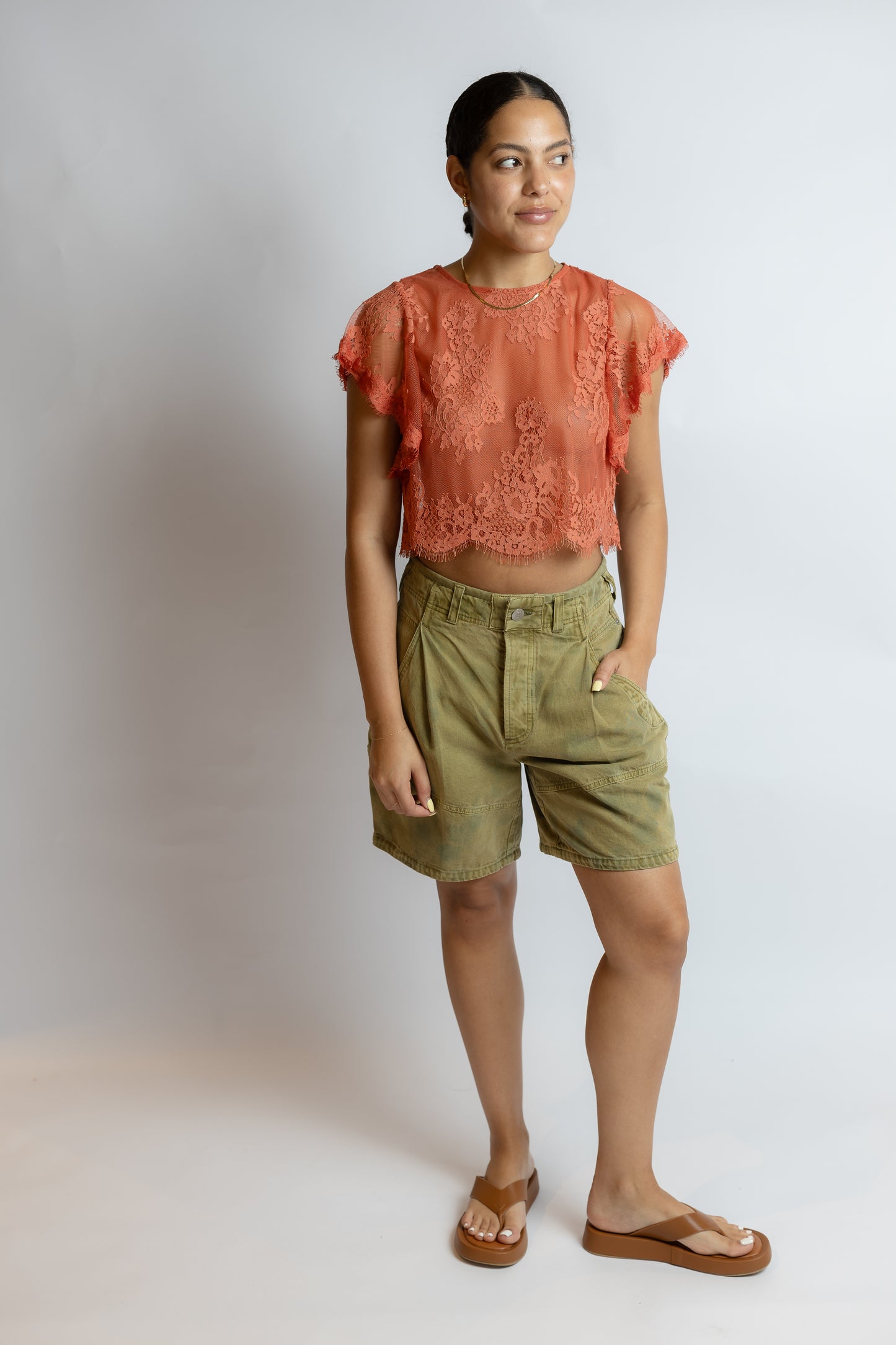Woman wearing a lace top and green shorts against a plain background