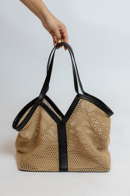 Beige mesh handbag with black trim held by a hand on a white background