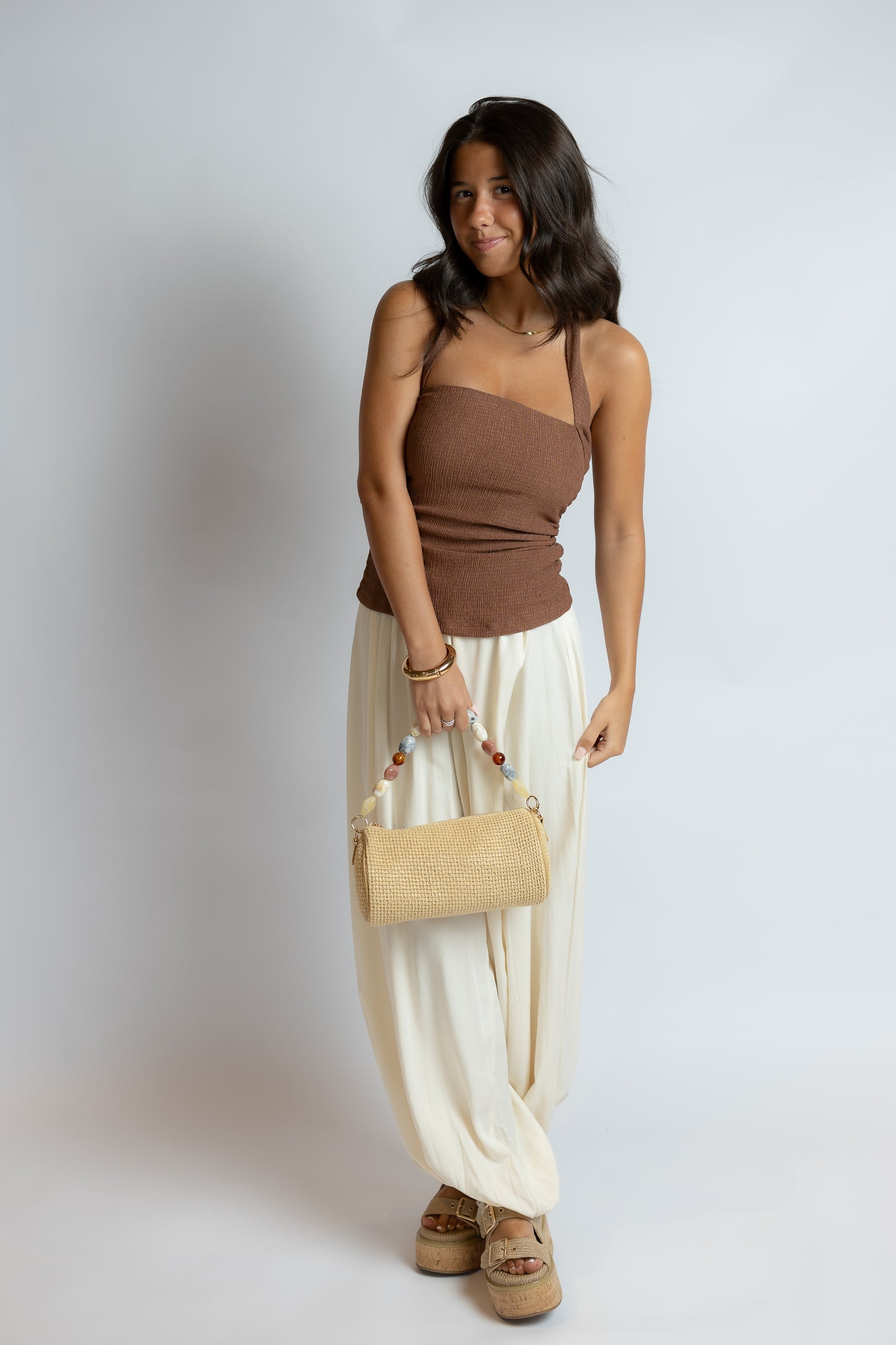 Woman holding a beige handbag against a plain background