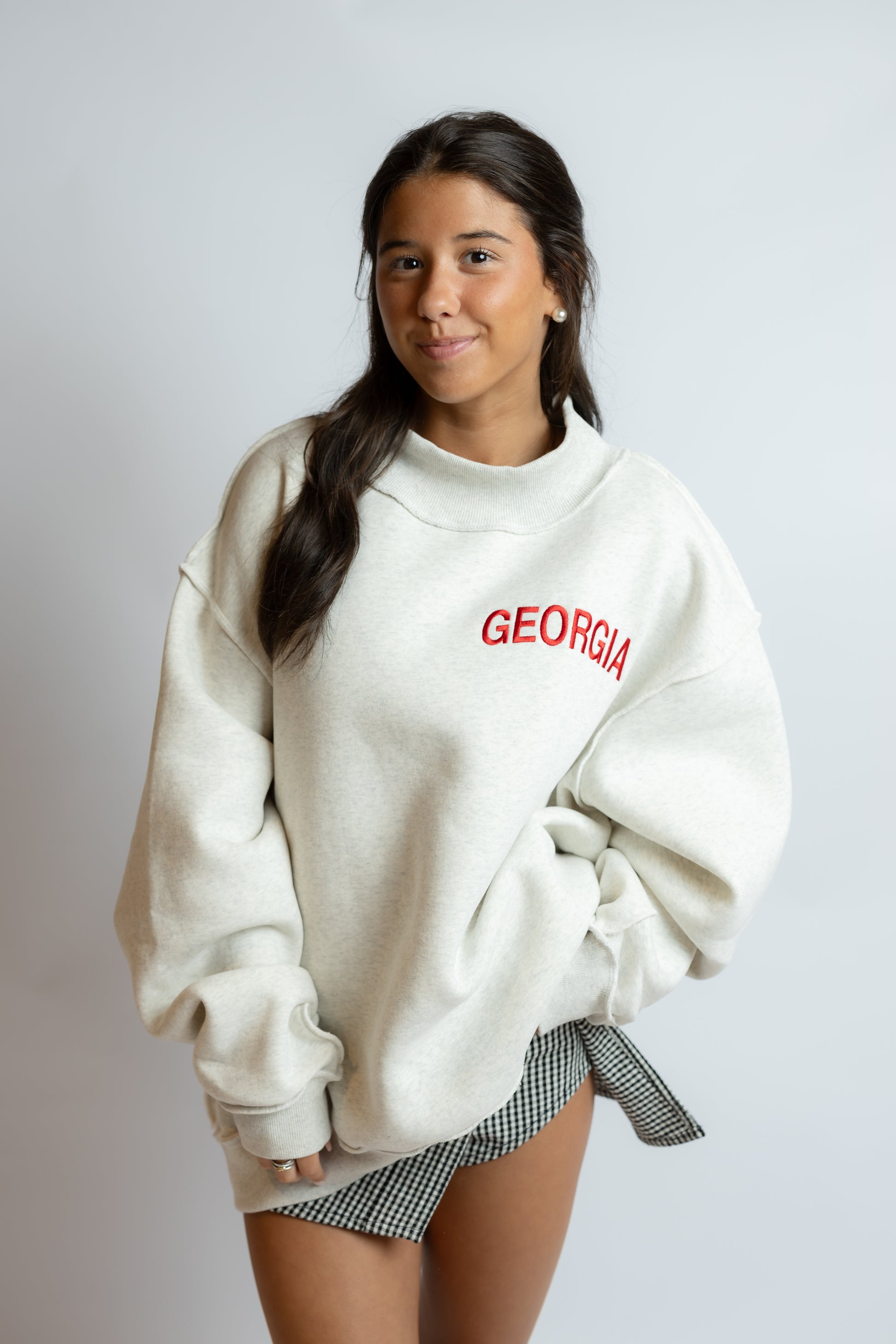 Woman wearing a white sweatshirt with 'GEORGIA' printed in red on a plain background
