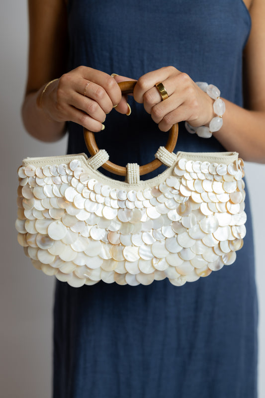 Person holding a white sequin handbag with wooden handle