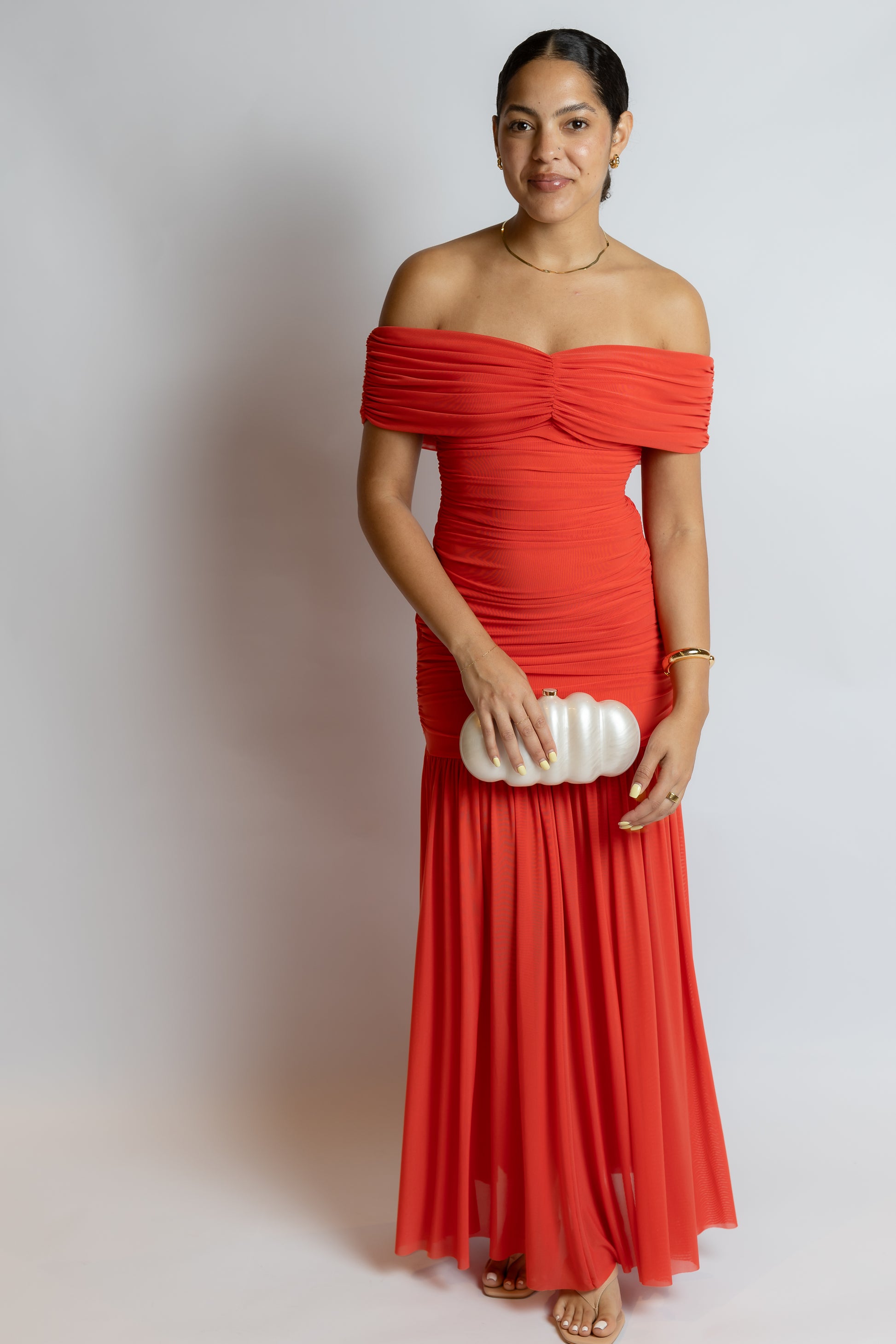 Woman wearing a red off-shoulder dress holding a white clutch against a plain background