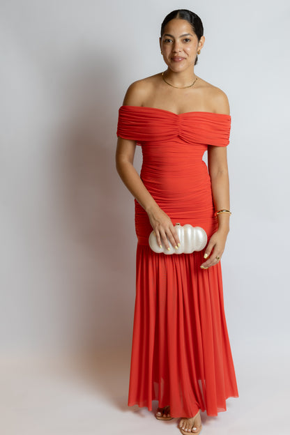 Woman wearing a red off-shoulder dress holding a white clutch against a plain background