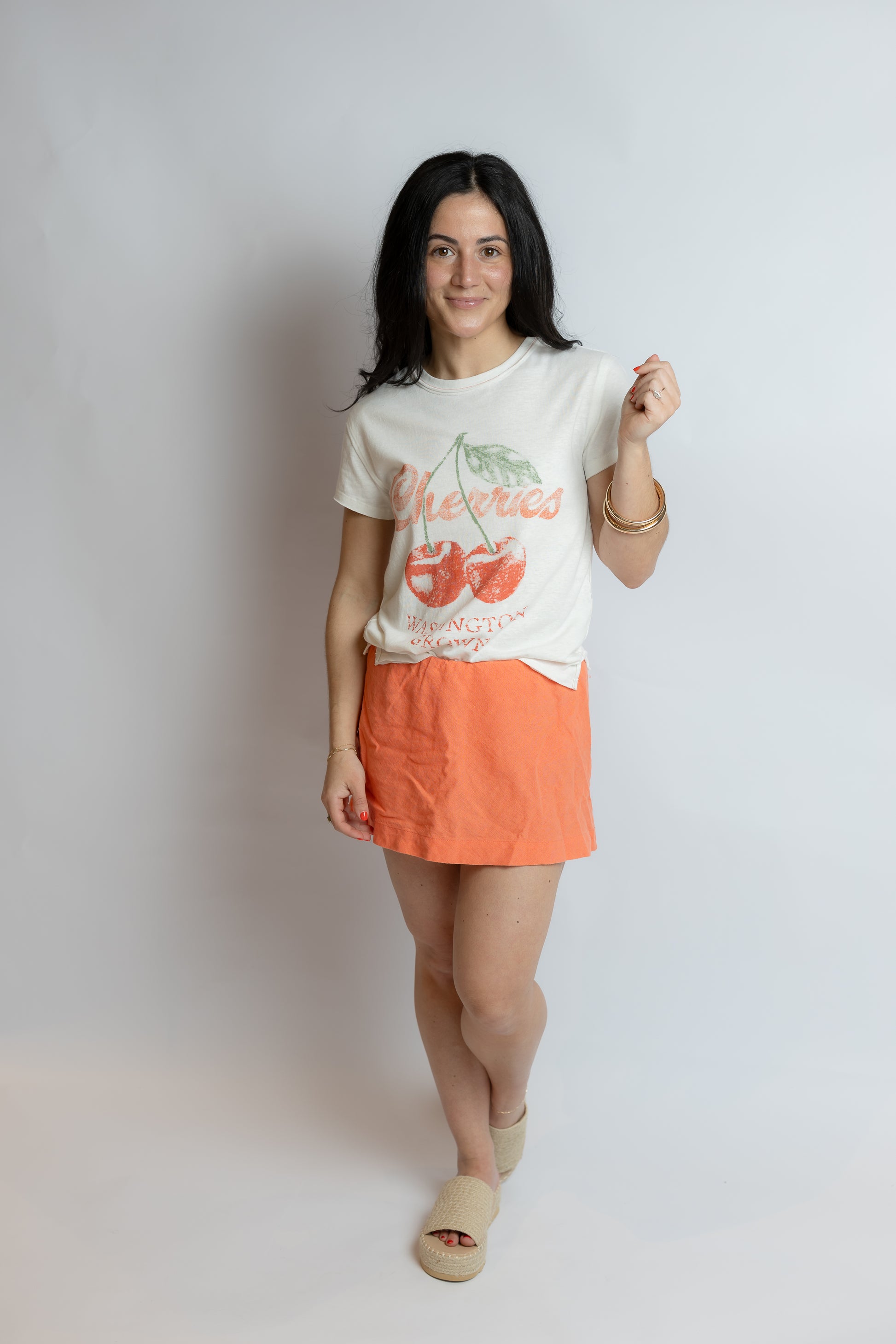 Woman wearing a white t-shirt with a graphic design and an orange skirt on a plain background