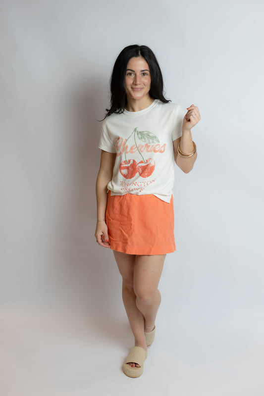 Woman wearing a white t-shirt with a graphic design and an orange skirt on a plain background