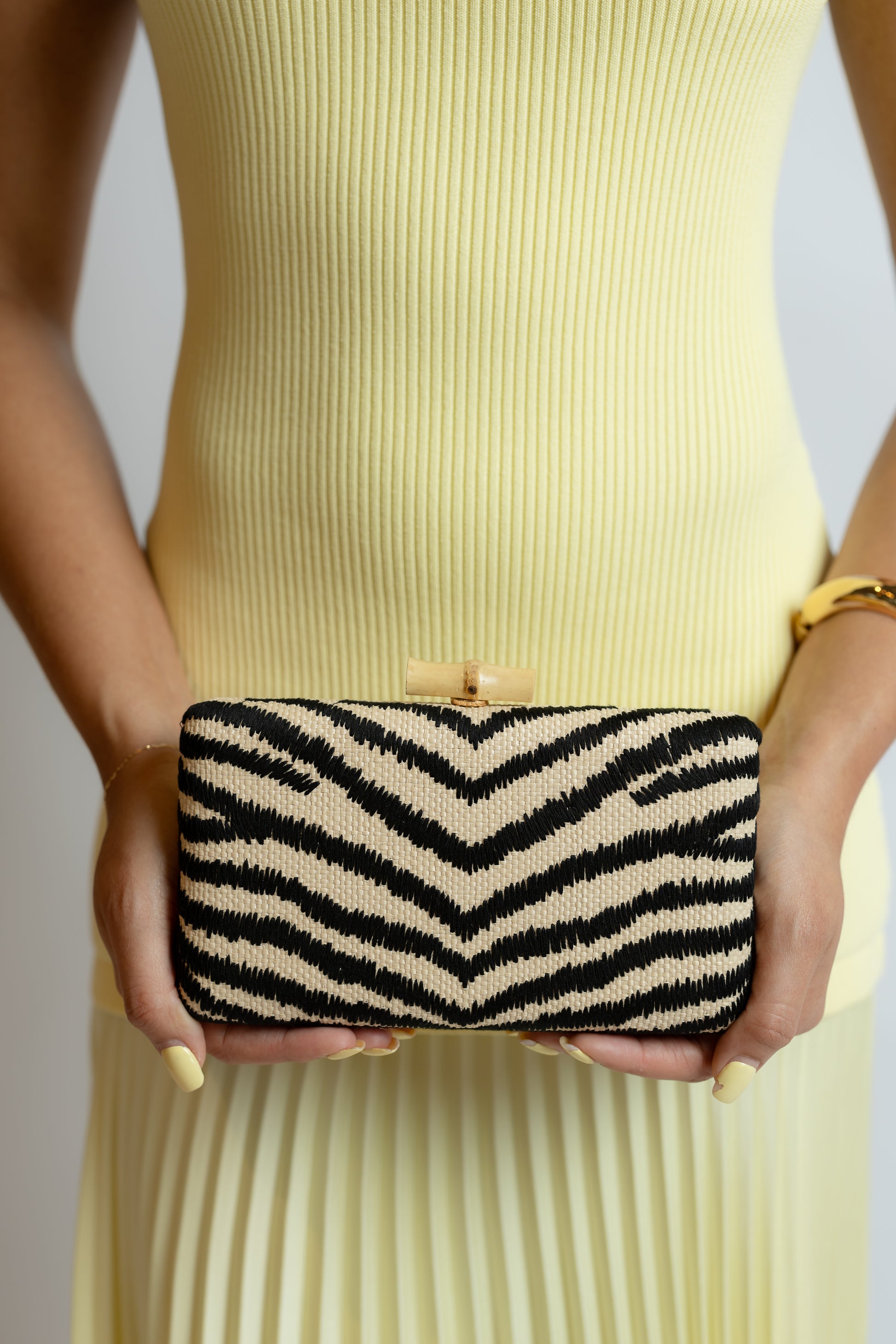 Person holding a black and white striped zebra clutch against a neutral background