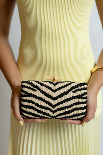 Person holding a black and white striped zebra clutch against a neutral background