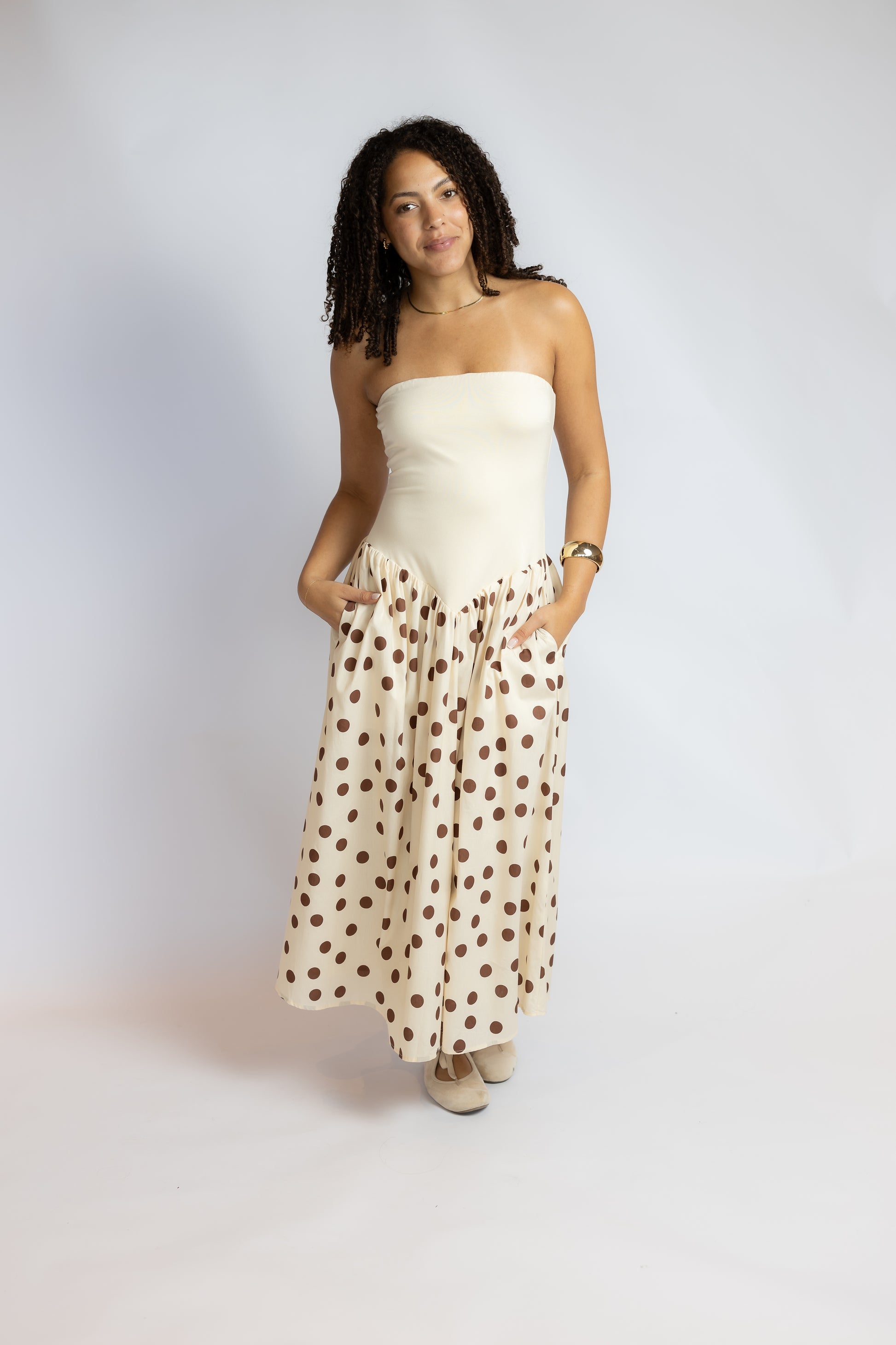A woman modeling a strapless tube top and matching maxi skirt set. The set features a solid cream-colored top and a skirt with brown polka dots on a cream background.