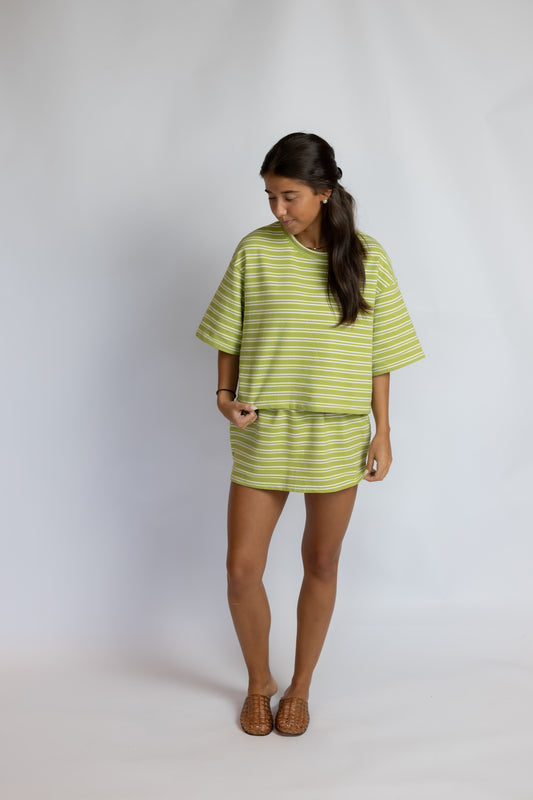 A woman modeling a lime green and white striped short-sleeve t-shirt dress against a light gray studio background.