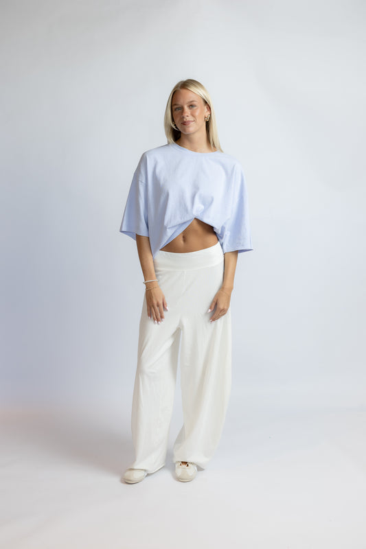 A woman modeling a light blue cropped t-shirt and white wide-leg trousers against a light gray studio background.
